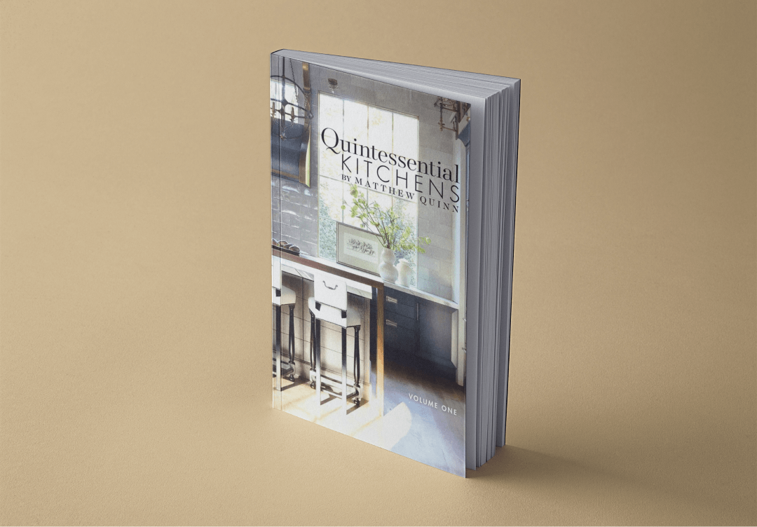 TOH1 3 (1) A book titled "Quintessential Kitchens" by Matthew Quinn, Volume One, stands upright on a light brown surface. Its cover features a photograph of a kitchen interior.